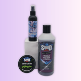 Three car care products displayed on a pale lavender gradient background: a black spray bottle labeled Ultra Violet standing on a white block, a large bottle of Squid HQ Pure HO Pure Vehicle Shampoo, and a round tin of Squid Custom Car Wax Afterglow in the foreground.