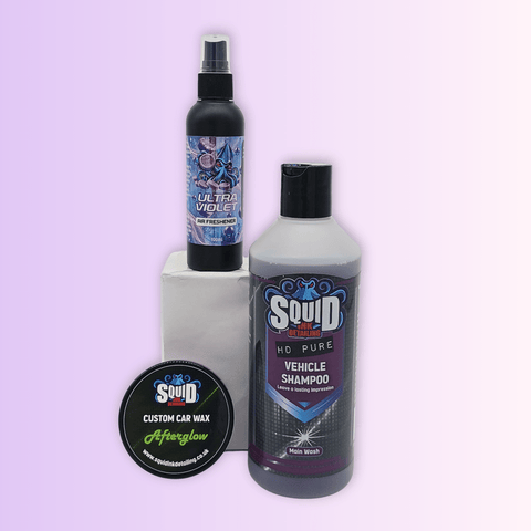 Three car care products displayed on a pale lavender gradient background: a black spray bottle labeled Ultra Violet standing on a white block, a large bottle of Squid HQ Pure HO Pure Vehicle Shampoo, and a round tin of Squid Custom Car Wax Afterglow in the foreground.