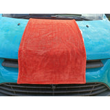 An orange, dual-sided, twisted loop drying towel laid out on the hood of a blue van.